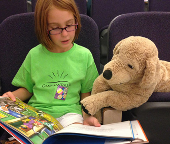 little girl reading a book with a stuffed animal dog